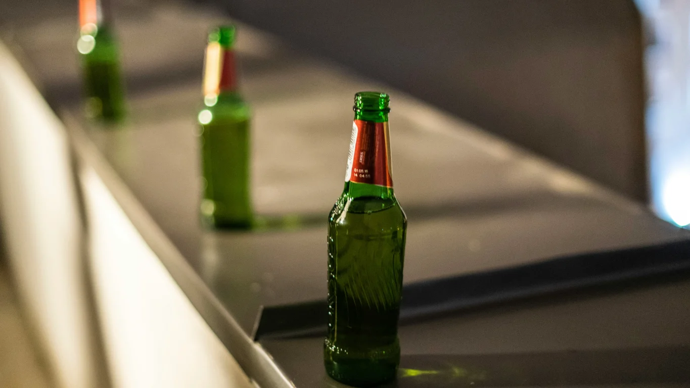 Drei grüne Bierflaschen hintereinander auf einer dunklen Metalltheke