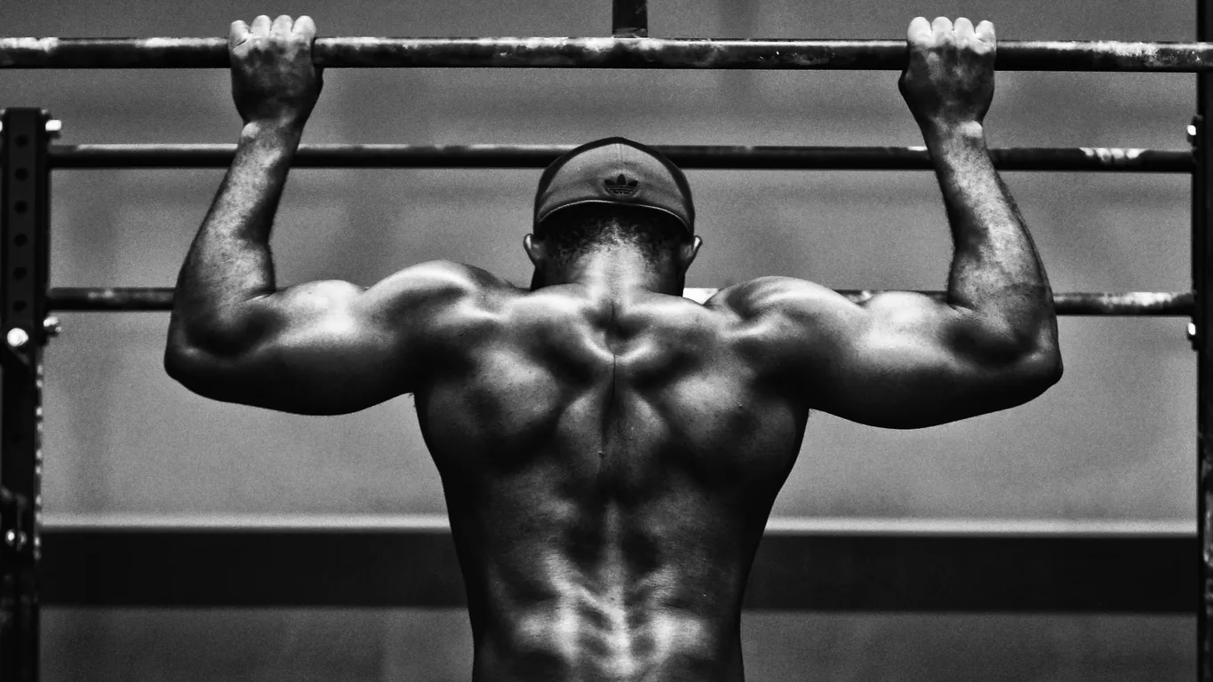 Man seen from behind doing a pull-up on a bar, back muscles in black and white