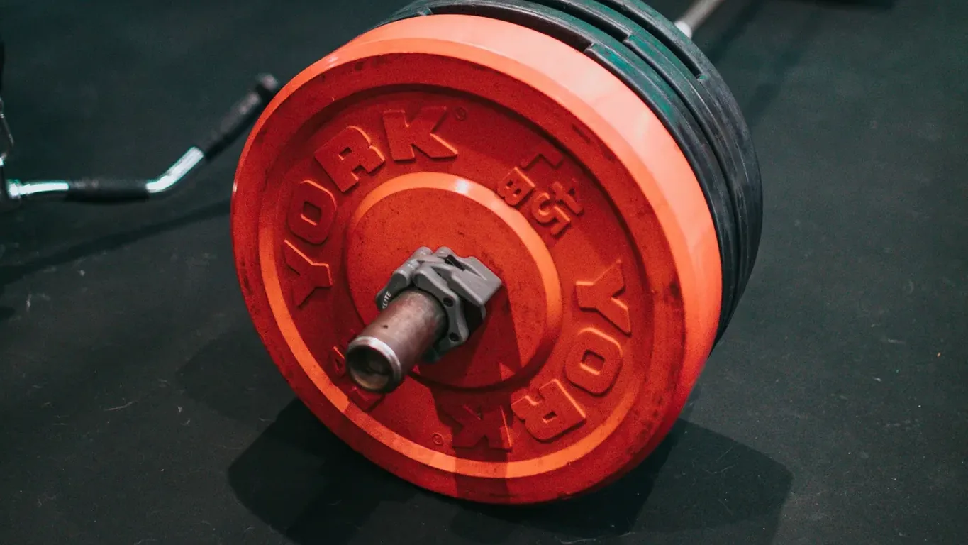 Beladene Langhantel mit roter Hantelscheibe auf dem Boden eines Fitnessstudios