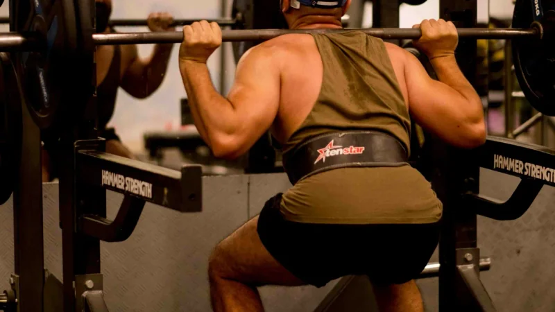 Gros plan sur des jambes en squat profond, genoux devant les orteils, sur une plateforme en bois
