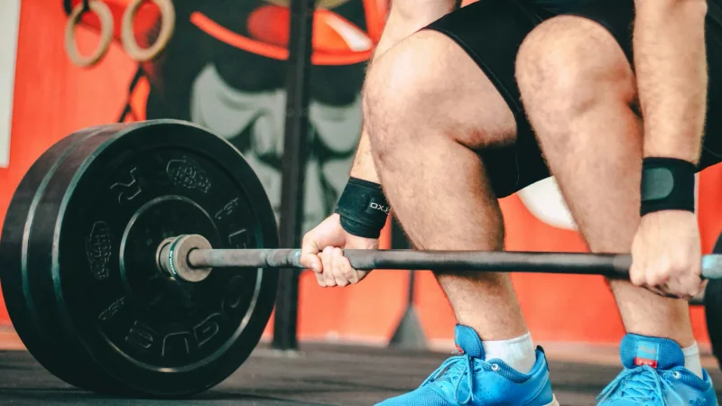 Barre, haltères et kettlebell côte à côte sur le sol d’une salle de sport, vus du dessus