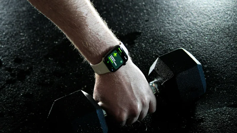 Hand mit Smartwatch an einer Kurzhantel auf dem Studioboden.