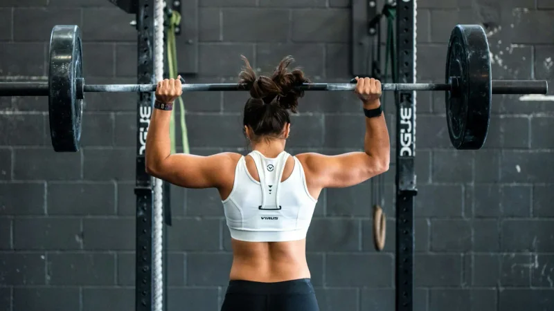 Femme effectuant un développé au-dessus de la tête à la barre, vue de dos dans une salle