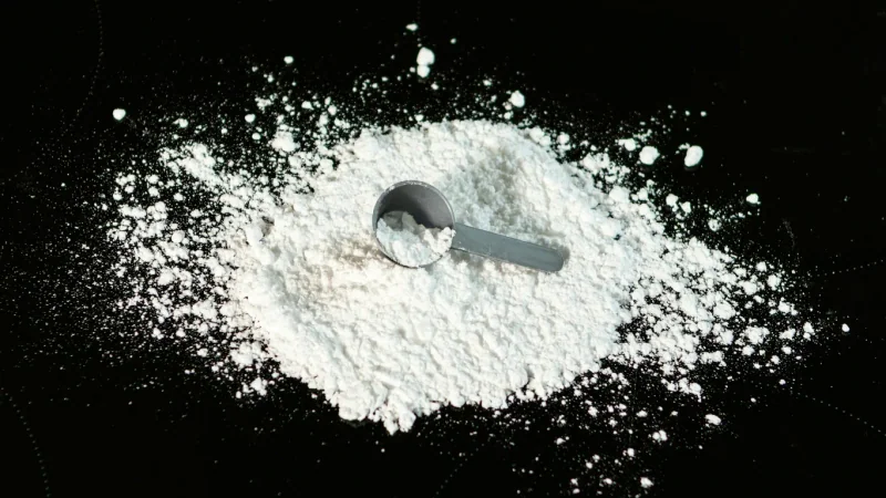 White powder with a measuring scoop on a dark surface.