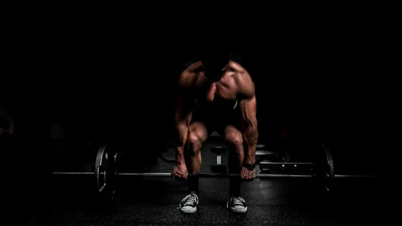 Young man sitting contentedly on a flat bench after training, loaded barbell in the rack behind him