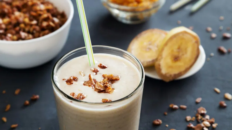 Smoothie topped with nuts beside banana slices and a bowl of muesli.