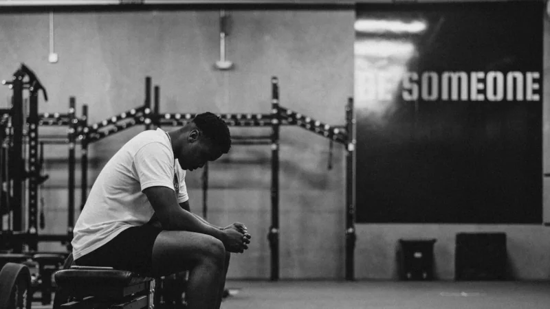 Homme assis sur un banc de musculation, penché en avant.