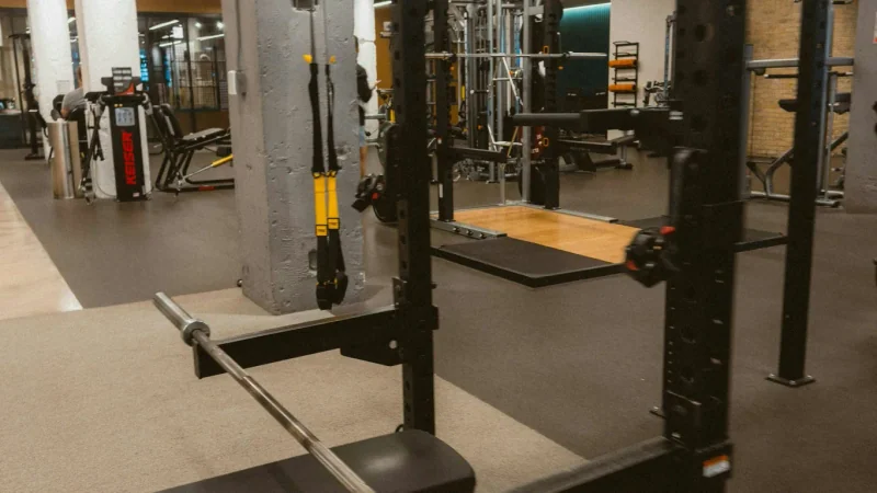 Homme effectuant un squat avec une barre dans un rack, vu de côté sous une lumière chaude