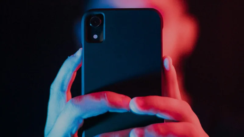 Hände halten ein Smartphone in rotem und blauem Licht.