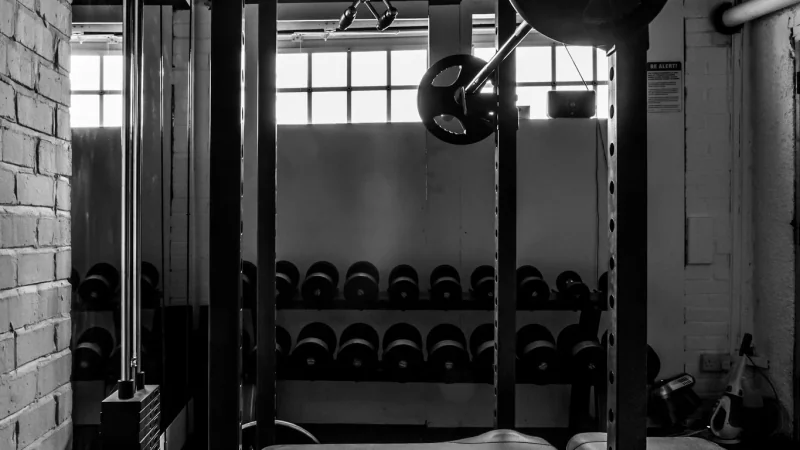 Homme pensif vu de dos devant un rack à squat, dans une lumière chaude