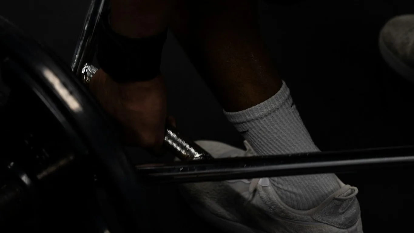Hand greift die Langhantel beim Kreuzheben-Setup, dunkles Gym, Nahaufnahme